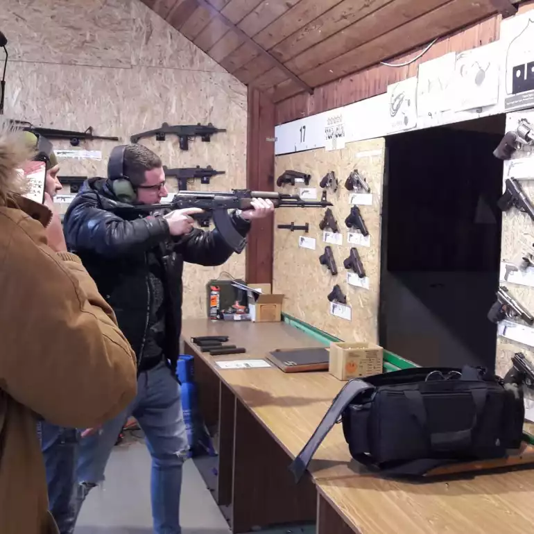 A person shooting a gun at a gun range in front of his friend.