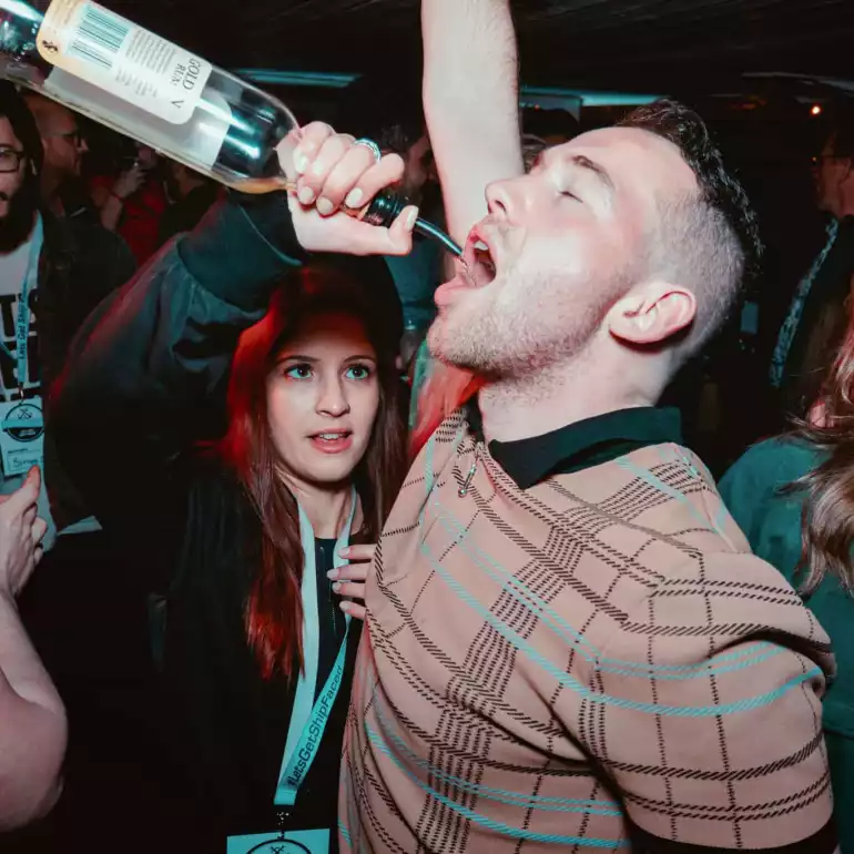 Guy in a sweater drinking from a bottle.