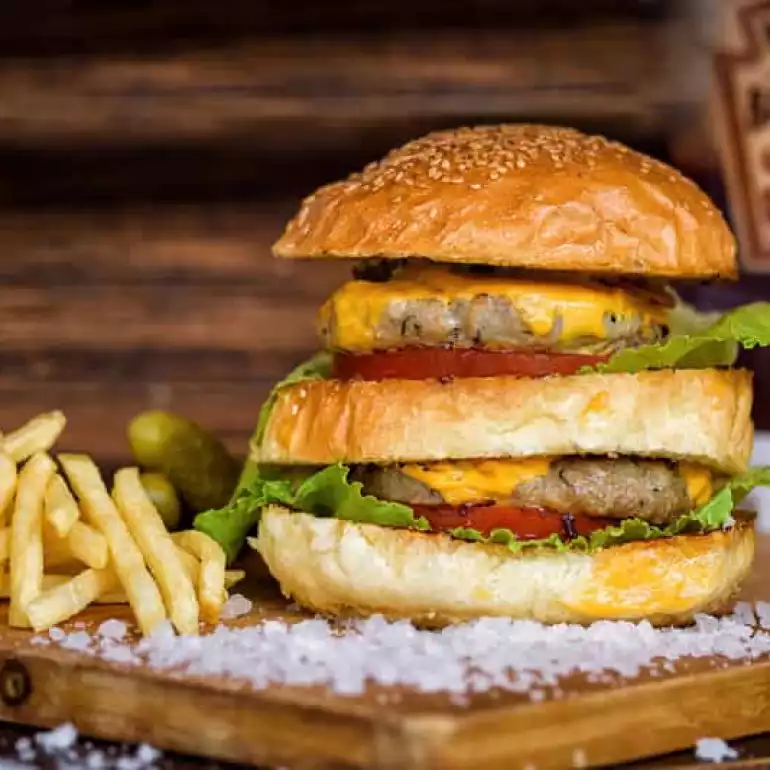 Juicy double cheeseburger with French fries and ketchup served on a wooden board.